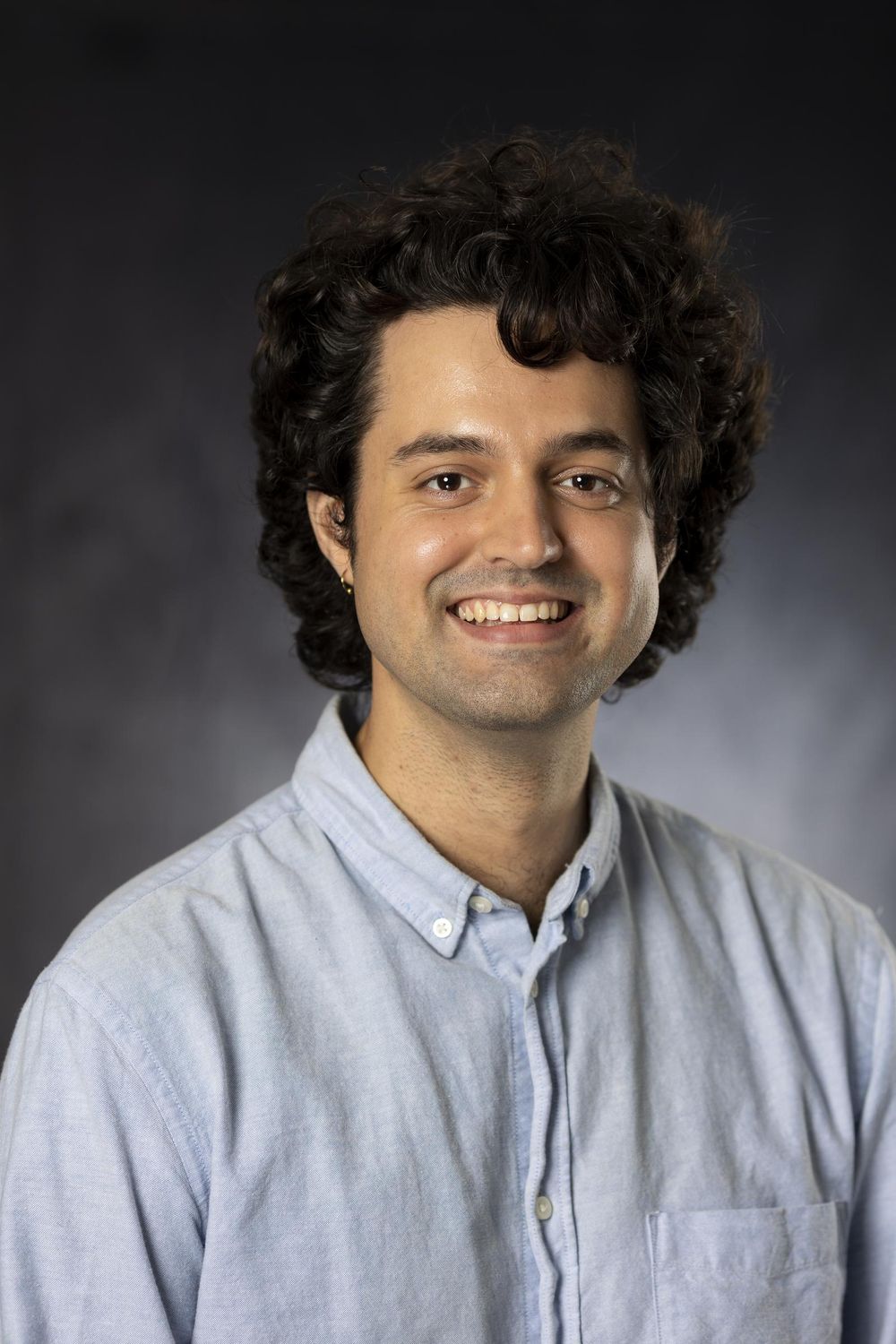 Business headshot of a man with dark curly hair in a light blue oxford shirt