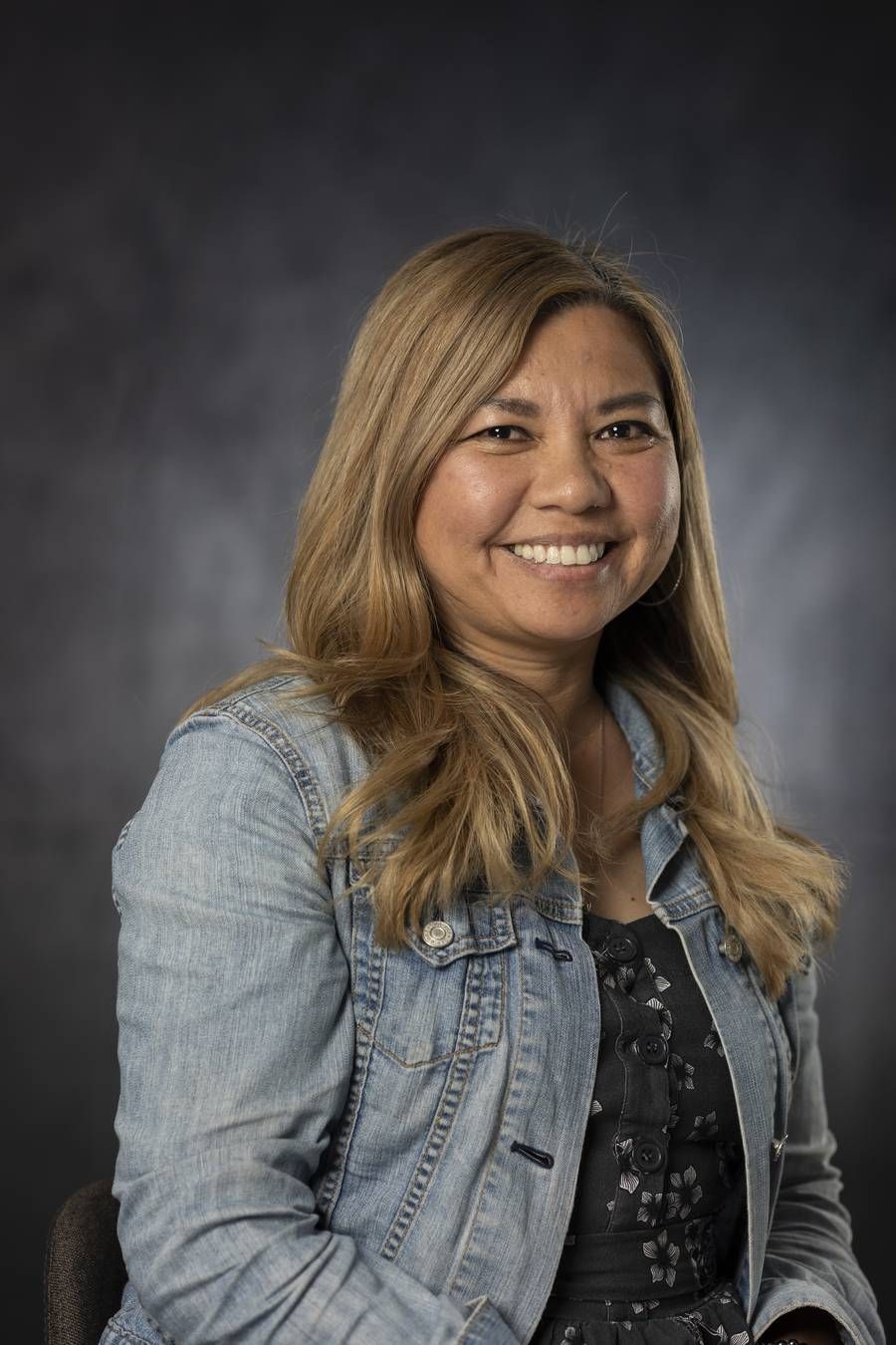 Business headshot of a woman with long highlighted hair in a denim jacket