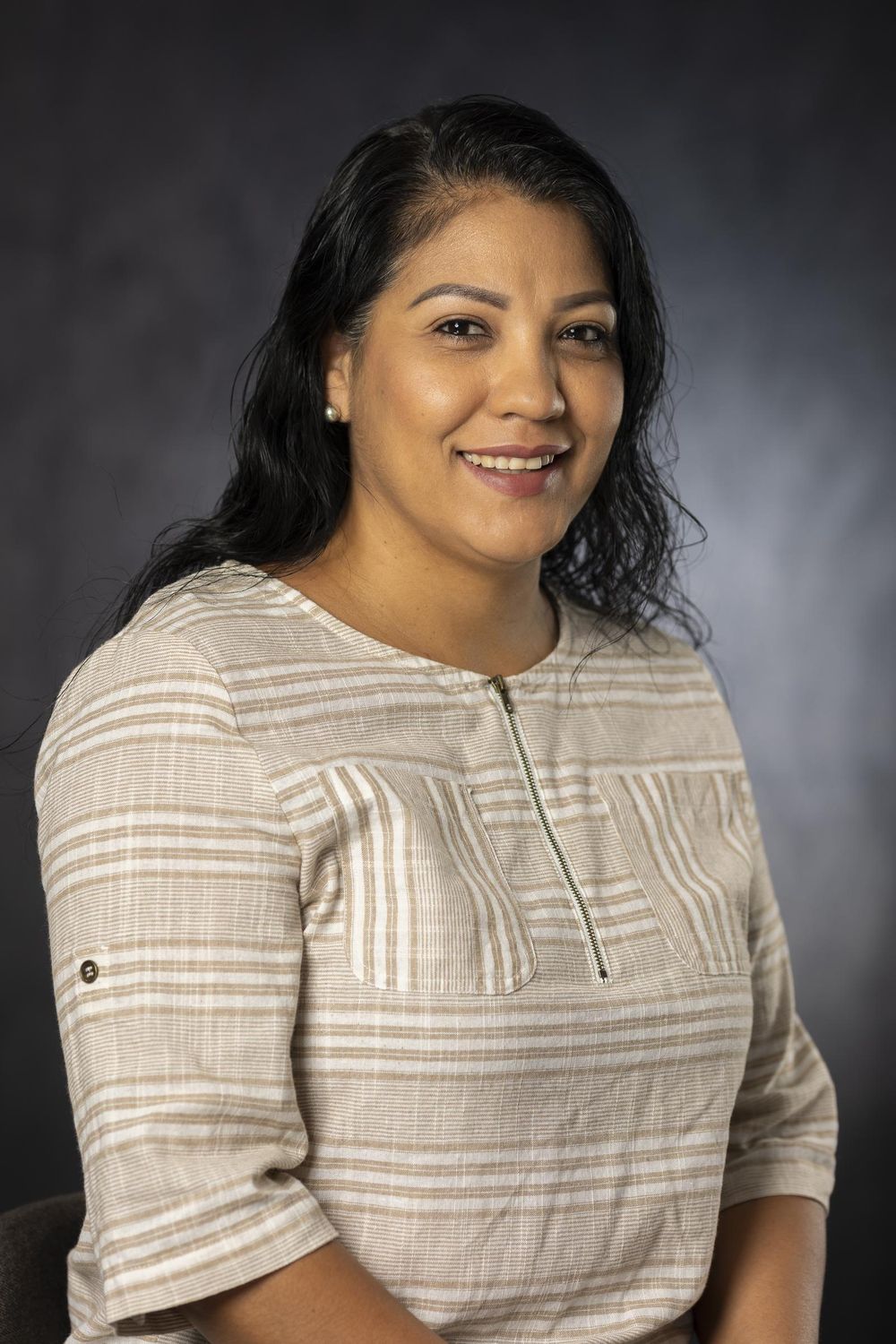 Business headshot of a woman in a striped knit top against a dark gray backdrop