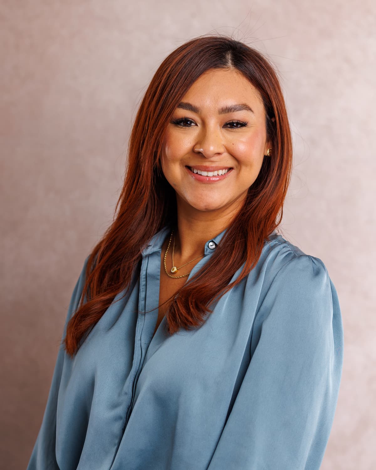 Executive in a blue satin blouse photographed in the studio against a soft blush backdrop