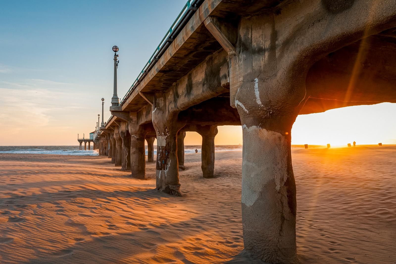 Sun flaring through the pilings of a Southern California pier at sunset over rippled sand